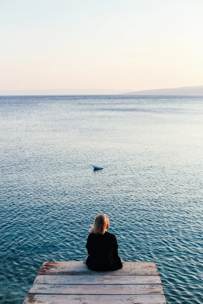 Person sitting alone on a dock looking out at the ocean
