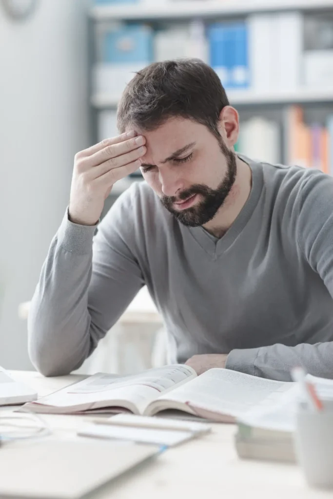 Man sitting at a desk with open books with a tense look on his face